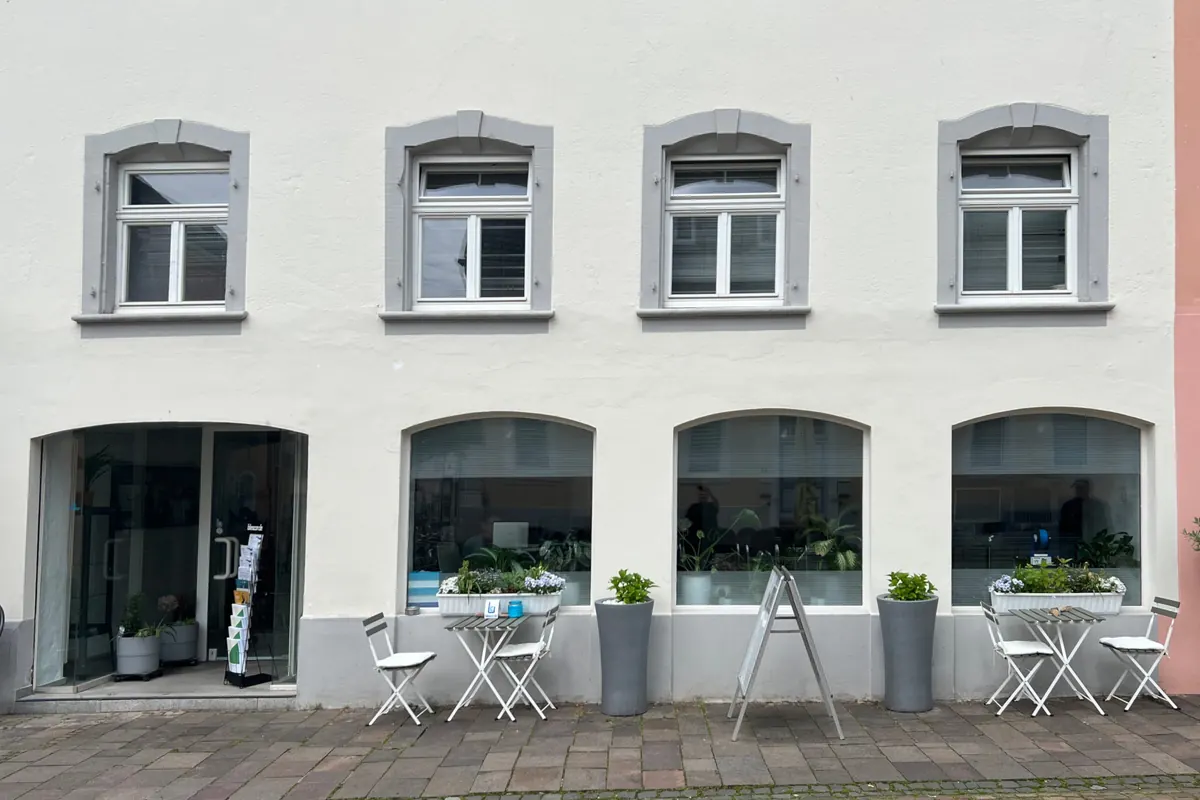 Das Büro der Bliestal Consulting in Blieskastel: helle Fassade mit Schaufenstern und Sitzplätzen vor dem Eingang.